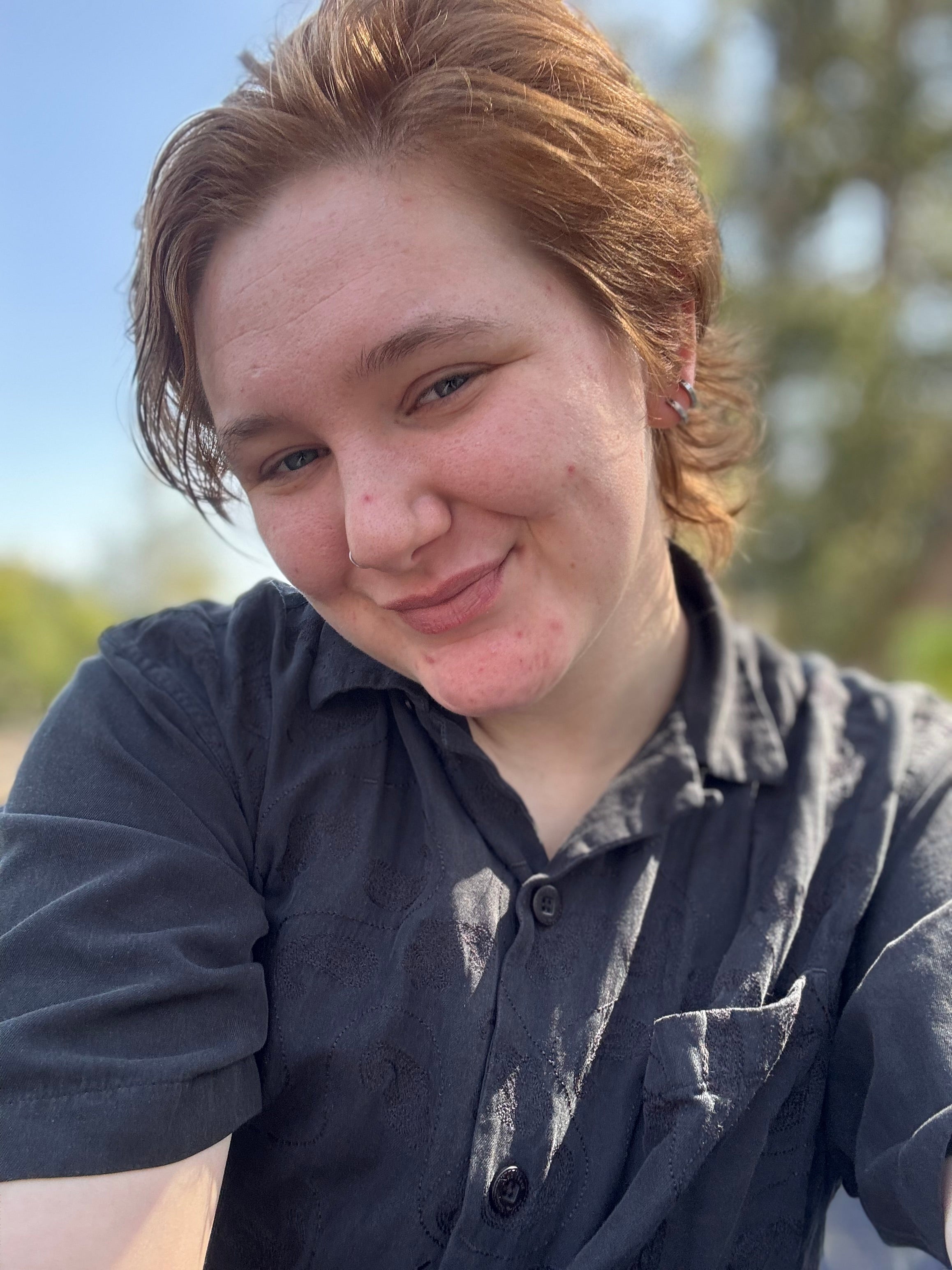 Person wearing a dark shirt outdoors with a blurred natural background